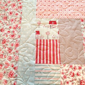 Peut inclure: Gros plan sur une courtepointe patchwork avec divers motifs de tissu. Comprend des imprim&eacute;s floraux rouges et gris, des rayures rouges et blanches et un motif &agrave; pois bleu clair. La courtepointe a un motif matelass&eacute;.