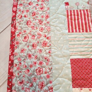 Peut inclure: Une courtepointe patchwork avec des motifs floraux, ray&eacute;s et &agrave; pois en rouge, bleu clair et blanc. La courtepointe a une bordure florale et est matelass&eacute;e avec un motif de feuilles. Le th&egrave;me g&eacute;n&eacute;ral est une esth&eacute;tique vintage et confortable.