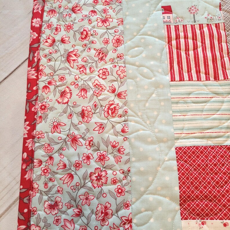 Peut inclure: Une courtepointe patchwork avec des motifs floraux, ray&eacute;s et &agrave; pois en rouge, bleu clair et blanc. La courtepointe a une bordure florale et est matelass&eacute;e avec un motif de feuilles. Le th&egrave;me g&eacute;n&eacute;ral est une esth&eacute;tique vintage et confortable.