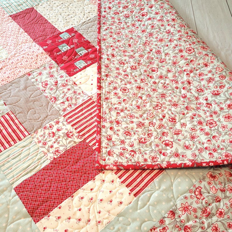 Peut inclure: Une courtepointe faite &agrave; la main avec un motif patchwork. La courtepointe pr&eacute;sente divers motifs rouges et blancs, notamment des rayures, des imprim&eacute;s floraux et des formes g&eacute;om&eacute;triques. Le dos est un motif floral avec une bordure rouge. Mesures en centim&egrave;tres.
