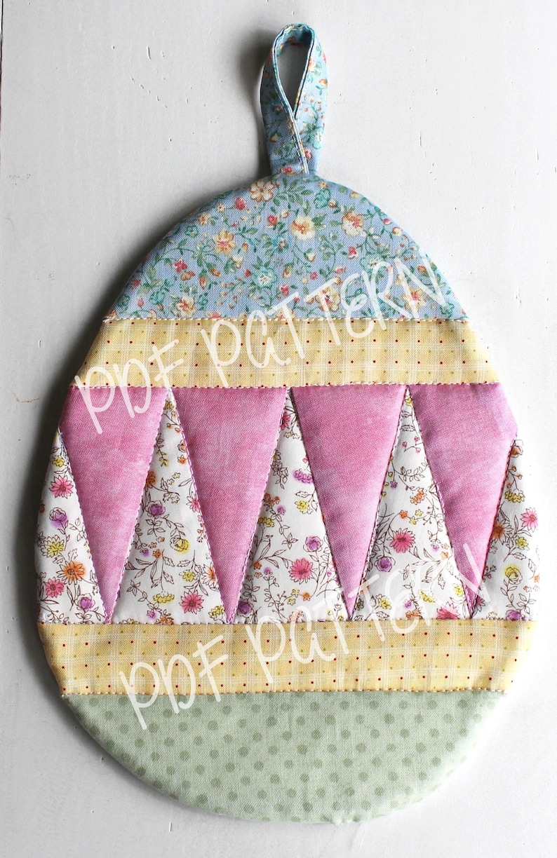 May include: A handmade quilted egg-shaped hot pad with a loop for hanging. The pad is made of various floral patterned fabrics in shades of blue, pink, yellow, and green.
