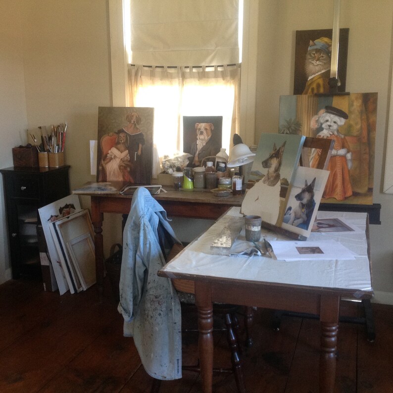 May include: A room with a wooden table and several paintings of dogs and cats. The paintings are propped up against the wall and on the table. There are also some paintbrushes and other art supplies on the table.