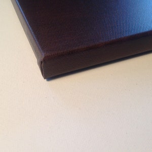 Pu&ograve; includere: Primo piano di una stampa su tela marrone scuro, che mostra l'angolo e il bordo. La tela &egrave; tesa su una cornice di legno, con una superficie strutturata. Lo sfondo &egrave; una superficie bianca.