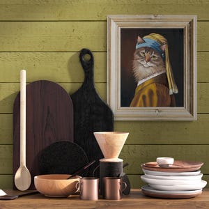 May include: A still-life arrangement featuring a framed painting of a cat in a yellow and blue headscarf, reminiscent of Vermeer's "Girl with a Pearl Earring." The scene includes wooden cutting boards, a wooden bowl, copper mugs, and a stack of white plates.