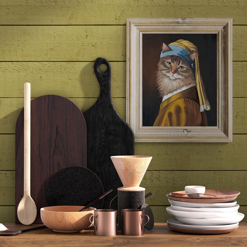 May include: A still-life arrangement featuring a framed painting of a cat in a yellow and blue headscarf, reminiscent of Vermeer's "Girl with a Pearl Earring." The scene includes wooden cutting boards, a wooden bowl, copper mugs, and a stack of white plates.