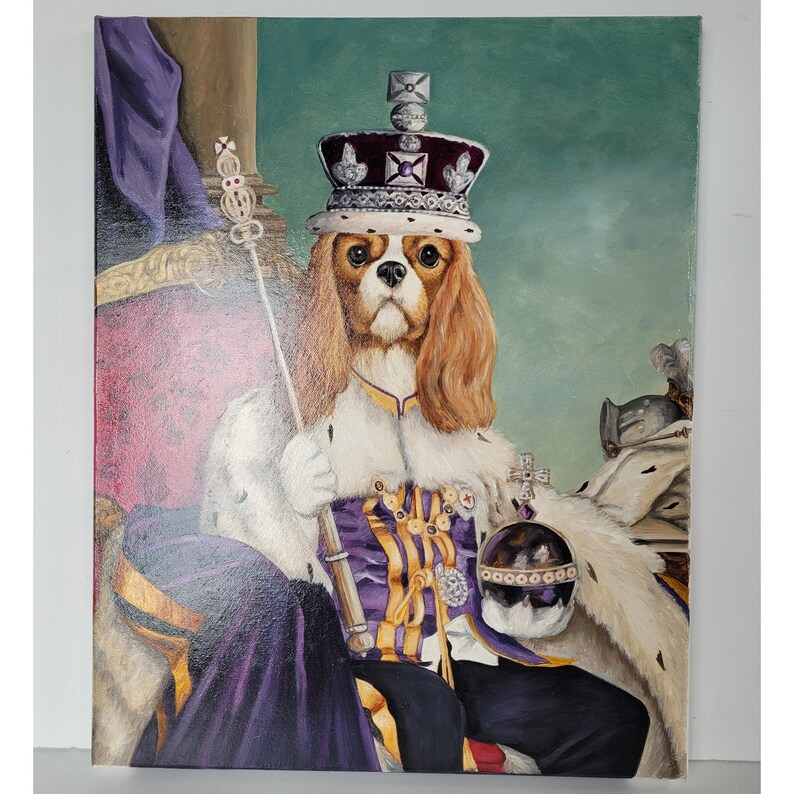 May include: A Cavalier King Charles Spaniel dog wearing a purple and gold royal robe and a crown with jewels. The dog is sitting on a throne with a purple and gold fabric. The background is a green wall.