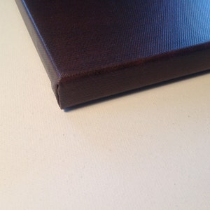 May include: Close-up of a dark brown canvas print. The canvas is stretched over a wooden frame, with the edges neatly folded and secured. The canvas has a textured surface, and the color is a deep, rich brown.