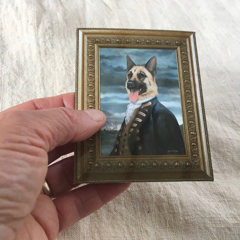 Peut inclure: Une peinture encadr&eacute;e d'un berger allemand v&ecirc;tu d'un uniforme d'amiral bleu marine et or, avec une cravate blanche et la langue rouge qui sort. Le chien est debout sur un fond de mer orageux avec un navire au loin.