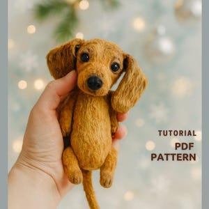 Può includere: Un peluche fatto a mano a forma di cane bassotto marrone, con orecchie flosce e una lunga coda. Il peluche è tenuto in mano su uno sfondo sfocato con il testo "TUTORIAL PDF PATTERN".
