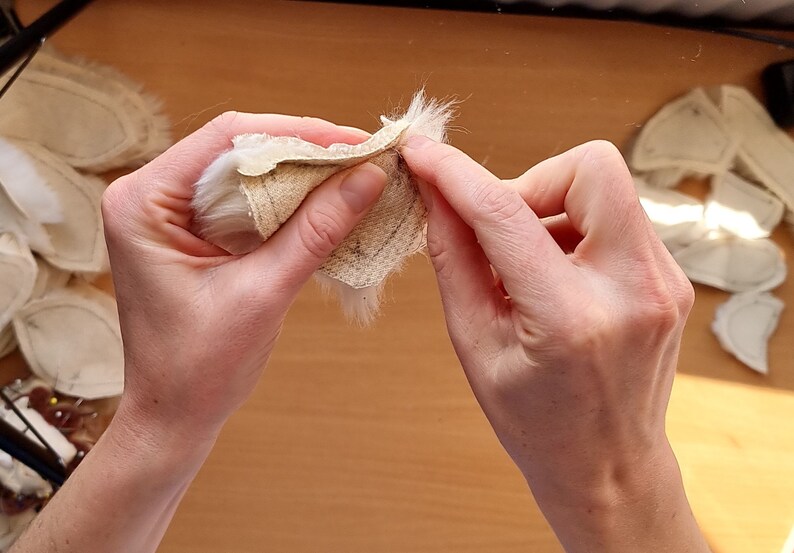 May include: A person is holding a white fur fabric with a beige backing. The fabric is folded in half and the person is holding the edges of the fabric.