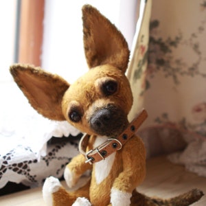 May include: A brown and white plush chihuahua dog toy with a brown leather collar. The toy is sitting on a wooden surface.