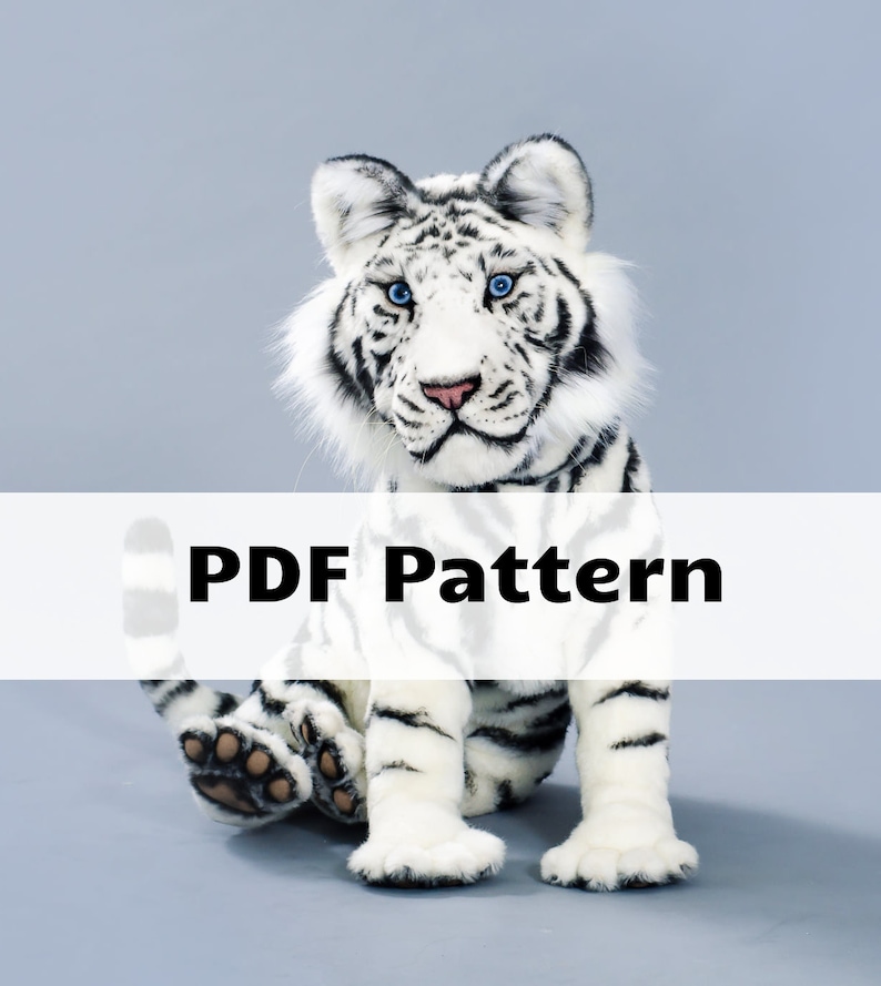 May include: A white tiger plush toy with black stripes, blue eyes, and brown paw pads. The toy is sitting on a gray background. PDF Pattern.