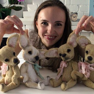 May include: Four handmade plush chihuahua dog toys. The toys are beige with pink and blue accents. The toys are sitting on a white surface.