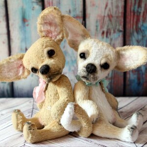 May include: Two plush chihuahua dog toys, one is cream colored with pink ears and a pink bow, the other is white with brown ears and a light blue bow.