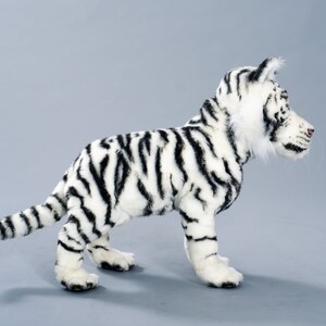 May include: A white stuffed tiger with black stripes. The tiger is standing on a gray background and is looking to the right.