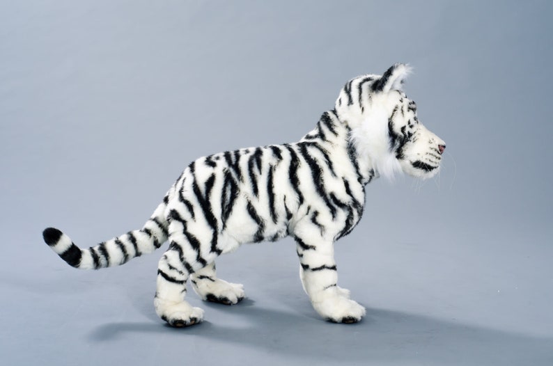 May include: A white stuffed tiger with black stripes. The tiger is standing on a gray background and is looking to the right.