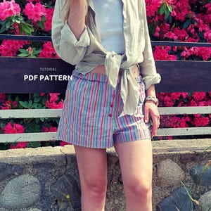 May include: Striped shorts with red, green, and blue vertical stripes. The shorts have a button closure and are part of a PDF pattern tutorial. The shorts are worn with a light green button-down shirt tied at the waist.