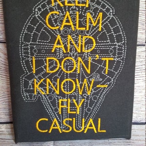 May include: Black canvas with yellow embroidered text that reads "Keep Calm and I Don't Know - Fly Casual" with a gray embroidered image of the Millennium Falcon in the background.