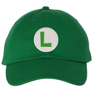 May include: A green baseball cap with a curved brim. The cap features a white circular patch with a green embroidered "L" in the center. The cap is made of a soft fabric and has a button on top.