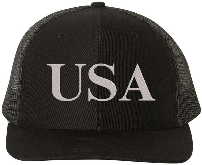 Pode incluir: Bon&eacute; de caminhoneiro preto e cinza com um "USA" bordado em branco na frente.