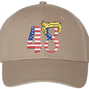 May include: A tan baseball cap featuring the number "48" embroidered on the front. The numbers are designed with the American flag pattern. Above the number "8" is a yellow and blue design.