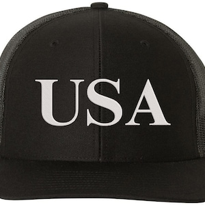 Pode incluir: Um bon&eacute; de caminhoneiro preto e cinza com uma malha branca nas costas. A frente do bon&eacute; tem a palavra "USA" bordada em branco.