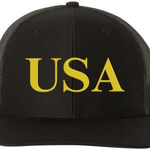 Pode incluir: Bon&eacute; de caminhoneiro preto com parte de tr&aacute;s em malha preta e "USA" bordado em amarelo na frente.