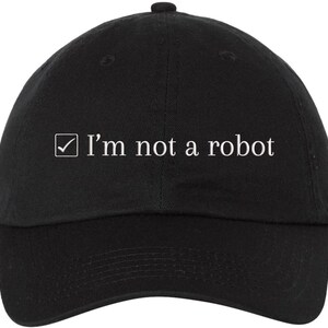 May include: Black baseball cap with the text "I'm not a robot" in white. The text is accompanied by a white checkmark inside a box. The cap has a curved brim and a button on top.