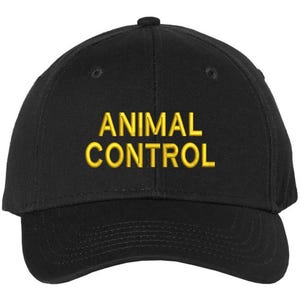 May include: Black baseball cap with the embroidered text "ANIMAL CONTROL" in yellow. The cap has a curved brim and a button on top. A classic, adjustable hat.