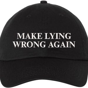 May include: Black baseball cap with the white text "MAKE LYING WRONG AGAIN" embroidered on the front. The cap has a curved brim and a button on top. The hat is made of a soft fabric.