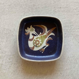 May include: A blue ceramic dish with a white rooster design. The rooster has brown, green, and yellow accents.