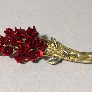 May include: A gold-toned brooch with a bouquet of red flowers and green leaves.