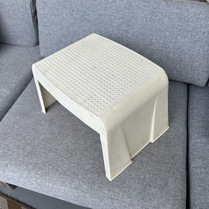 May include: A white plastic step stool with a textured surface. The stool has a rounded top and a rectangular base.