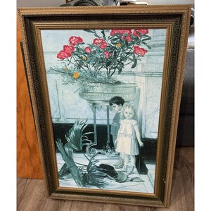 May include: A framed print featuring a vintage illustration of two children standing near a large decorative planter filled with red flowers and greenery. The frame is gold with ornate detailing, adding to the artwork's antique aesthetic.