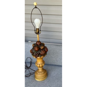 May include: A wooden table lamp with a fruit motif. The lamp base is shaped like a vase and features carved grapes, pears, and apples. The lampshade is white and has a simple design.