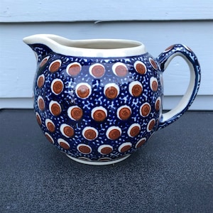 May include: A blue and brown ceramic pitcher with a polka dot pattern. The pitcher has a round body and a handle.
