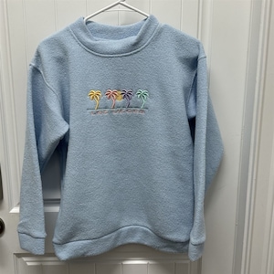 May include: A light blue sweatshirt with a colorful palm tree graphic and the text "Las Vegas" embroidered on the front.