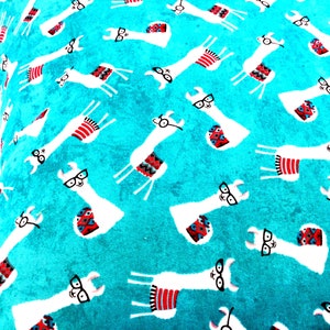 May include: A bright turquoise fabric featuring a repeating pattern of white llamas wearing black-rimmed glasses. Each llama is adorned with a small, colourful saddle blanket in shades of red, blue, and black, arranged in various orientations.