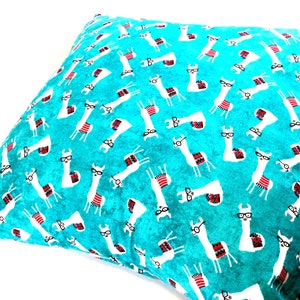 May include: A square throw cushion featuring a vibrant turquoise background with a repeating pattern of white llamas. Each llama is illustrated wearing black-rimmed glasses and a colourful patterned saddle blanket in shades of red, blue, and white.