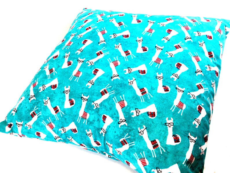 May include: A square throw cushion featuring a vibrant turquoise background with a repeating pattern of white llamas. Each llama is illustrated wearing black-rimmed glasses and a colourful patterned saddle blanket in shades of red, blue, and white.