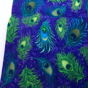 May include: Close-up of a fabric with a repeating peacock feather pattern. The feathers are in shades of green, blue, and gold against a deep purple background. The design is detailed and vibrant, suggesting a textile or decorative item.