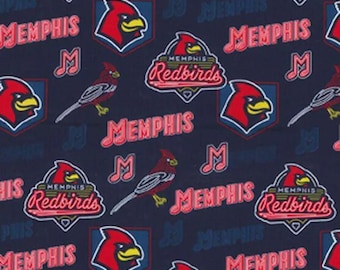 May include: A dark blue fabric featuring a repeating pattern of the Memphis Redbirds baseball team logo, including the red cardinal bird head, the team name in red text, and musical note symbols, with a ruler showing centimetres at the bottom.