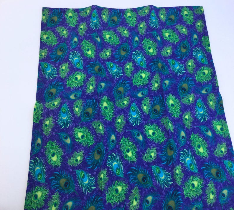 May include: A fabric with a repeating pattern of peacock feathers in shades of green, blue, and yellow on a dark purple background. The feathers are detailed with eye-like patterns.