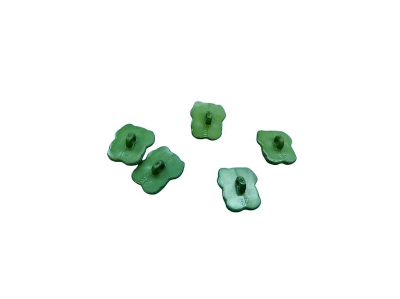 Puede incluir: Cinco botones peque&ntilde;os de color verde claro con forma de cuatro l&oacute;bulos similar a un tr&eacute;bol. Cada bot&oacute;n presenta un ojal central en la superficie superior para su fijaci&oacute;n. Los botones tienen un acabado mate y liso, dispuestos dispersos.