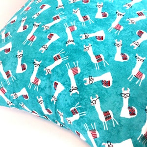 May include: A square throw cushion featuring a vibrant turquoise background with a repeating pattern of white llamas. Each llama wears black-rimmed glasses and a colourful patterned saddle blanket in shades of red, blue, and grey.