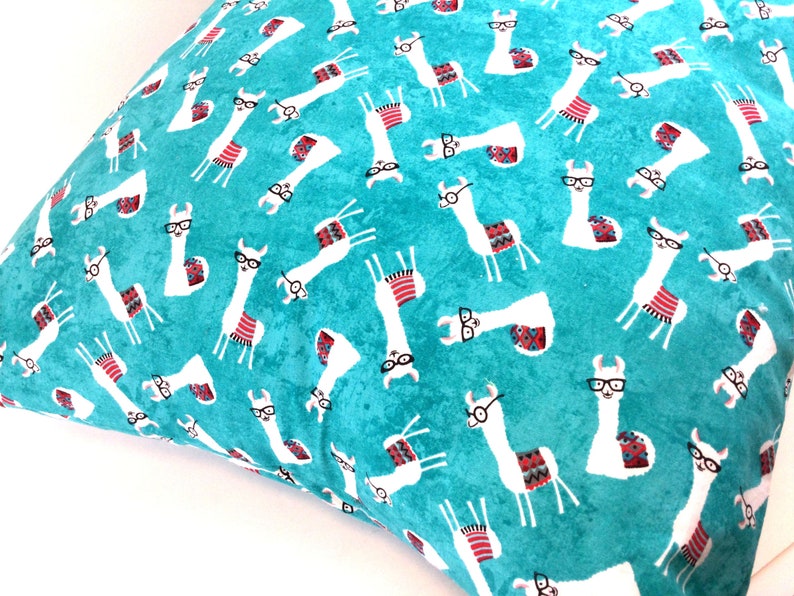 May include: A square throw cushion featuring a vibrant turquoise background with a repeating pattern of white llamas. Each llama wears black-rimmed glasses and a colourful patterned saddle blanket in shades of red, blue, and grey.