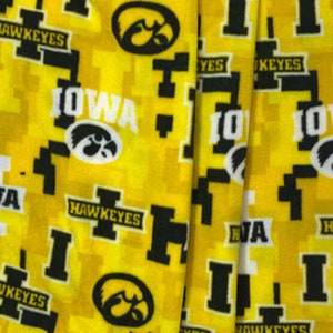 May include: Yellow fabric with a repeating pattern of the University of Iowa logo, the word "Iowa", and the words "Hawkeyes".