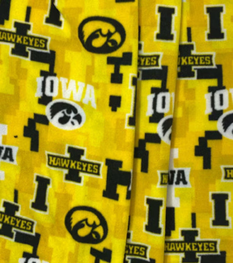 May include: Yellow fabric with a repeating pattern of the University of Iowa logo, the word "Iowa", and the words "Hawkeyes".