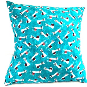 May include: A square throw cushion featuring a vibrant turquoise background with a repeating pattern of white llamas. Each llama is depicted wearing black-rimmed glasses and a small red and white striped blanket draped across its back.
