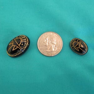 May include: Two black oval buttons with gold designs, and a U.S. quarter coin. The buttons feature a sun-like design. The buttons are on teal fabric.
